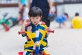 Asian boy rides tricycle at playground. Cute baby wearing colorful dress is sweating on his face due to hot weather. Royalty Free Stock Photo