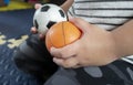 Asian boy sitting on foam carpet in living room and in his hands holding soccer balls and basketball Royalty Free Stock Photo