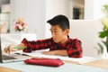 Asian boy sitting at table and using laptop during online lessons Royalty Free Stock Photo