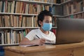 Asian boy student wearing protective mask learning studying online with laptop computer in library, school from home Royalty Free Stock Photo