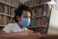 Asian boy student wearing protective mask learning studying online with laptop computer in library, school from home Royalty Free Stock Photo