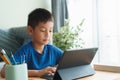 Asian boy is studying online via the internet on tablet while sitting in the living room in morning, Asia child watching and Royalty Free Stock Photo