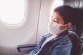 Asian boy wear face mask sit on passenger economy seat near cabin window in airplane