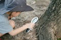 Asian boy wearing a hat in a forest exploration suit Use a magnifying glass to survey the tree area