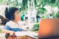 Asian boy wearing headphones concentrated learning with laptop computer and doing homework. Royalty Free Stock Photo