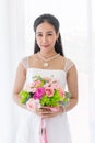 An Asian bride dressed in a white wedding dress stands smiling brightly in a hand holding a beautiful flower bouquet Royalty Free Stock Photo