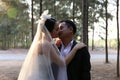 Asian bride in lovely wedding dress kisses her groom in a pine forest