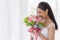An Asian bride in a wedding dress is sitting smiling brightly on the bed in her hand holding a beautiful bouquet of flowers Royalty Free Stock Photo
