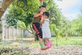 Asian brother and sister having fun playing with outdoor tree hanging rope swing toy at backyard Royalty Free Stock Photo