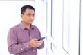 Asian business man is holding smartphone mobile phone in his hand and look out from window in the room Royalty Free Stock Photo