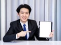 Asian business man wearing suit, pointing to tablet or smartphone. Royalty Free Stock Photo