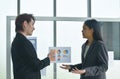 Asian business man and woman looking at paper note stick on glass board to discuss and working in office Royalty Free Stock Photo