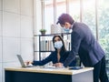 Asian business man and woman wearing suit and protective face masks using computer on desk, meeting and working together in office Royalty Free Stock Photo