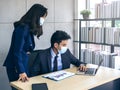 Asian business man and woman wearing suit and protective face masks using computer on desk, meeting and working together in office Royalty Free Stock Photo