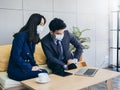 Asian business man and woman wearing suit and protective face masks using computer on desk, meeting and working together in office Royalty Free Stock Photo