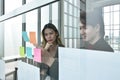 Asian business man and woman looking at paper note stick on glass board to discuss and working in office Royalty Free Stock Photo