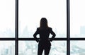 Asian business woman with arms akimbo looking out the window at city view background Royalty Free Stock Photo