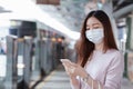 Asian business woman in casual dress code wearing face mask using mobile phone. She is waiting for the train to go to work on the Royalty Free Stock Photo