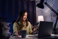 Asian business woman drinking water or coffee is using computer and smartphone to work in the evening at home Royalty Free Stock Photo