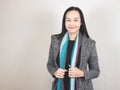 Asian business woman with long black hair, wearing scarf and winter coat, standing on white background smiling and looking at