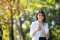 An Asian business woman is relaxing with her smartphone and coffee in the park, with a blurred background.