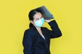 Asian business woman wearing medical shielding mask with laptop computer on her head isolated on yellow background Royalty Free Stock Photo