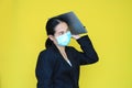 Asian business woman wearing medical shielding mask with laptop computer on her head isolated on yellow background Royalty Free Stock Photo