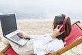 Asian business woman working with laptop while using headphones sitting in the beach chair on beach Royalty Free Stock Photo