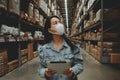 Asian business working woman wear mask using digital tablet checking stock of products in warehouse