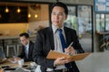 Asian businessman holding a book and pen to write a business plan. He standing and looking forward, thinking for business future Royalty Free Stock Photo