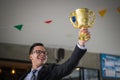 Asian businessman raising up hand and holding a golden trophy cup to cheerful and celebrated his successful in career and mission. Royalty Free Stock Photo