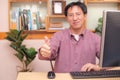 Asian Businessman showing thumbs up while using computer in home office, recommending best choice for business, good idea, great