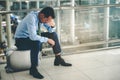 An Asian businessman is sitting on his luggage. He was stressed and looked at his smartphone at the airport