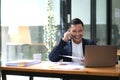 Asian businessman sitting on the phone with a customer with a laptop and document at his office desk. Royalty Free Stock Photo