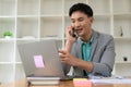 Asian businessman using smartphone and working at office desk using laptop and talking on mobile phone, Royalty Free Stock Photo