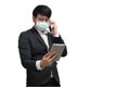 Asian businessman wearing surgical face mask in formal black suit jacket, using smartphone and tablet Royalty Free Stock Photo