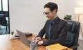 Asian businessman working on laptop in office. Successful Asian business man working on computer while sitting at desk. Smiling Royalty Free Stock Photo