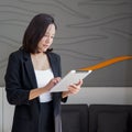 Asian businesswoman in black suit standing with tablet computer in her hand. Atmosphere of working outside the office during the Royalty Free Stock Photo