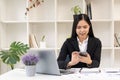 Asian businesswoman in a formal suit in the office and using a smartphone to work with a laptop to analyze financial graphs with a Royalty Free Stock Photo