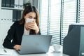 Asian businesswoman in formal suit wear facemask and work at workplace. Attractive female employee office worker sit on table, use