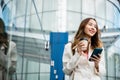 Asian businesswoman with smartphone and cup coffee standing against street building near office Royalty Free Stock Photo