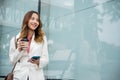 Asian businesswoman with smartphone and cup coffee standing against street building near office Royalty Free Stock Photo