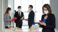 An Asian businesswoman in suit standing with mobile phone in her hand. The team is preparing for the meeting in the background. Royalty Free Stock Photo