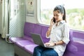 Asian businesswoman talking on cellphone and working on laptop while traveling by sky train. Business travel concept