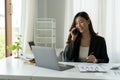 Asian Businesswoman Talking On Mobile Phone Working On Laptop for financial In Modern Office. Royalty Free Stock Photo