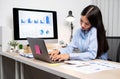 Asian businesswoman talking on the phone and working on a laptop with a cheerful and happy smile while working at the office