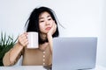 Asian businesswoman tired of working at office desk hand holding coffee mug looking at laptop lack of energy