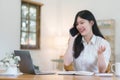 Asian businesswoman using laptop computer holding a mobile phone while working remotely from her home office. Royalty Free Stock Photo