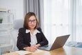 Asian businesswoman wearing suit and glasses writing notes book and working laptop on wooden table at home. Entrepreneur woman Royalty Free Stock Photo