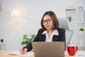 Asian businesswoman wearing suit and glasses writing notes book and working laptop on wooden table at home. Entrepreneur woman Royalty Free Stock Photo